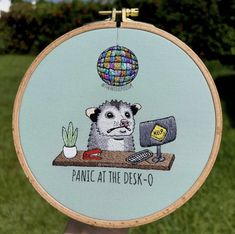 a person holding up a cross - stitch hoop with an image of a ferret on it