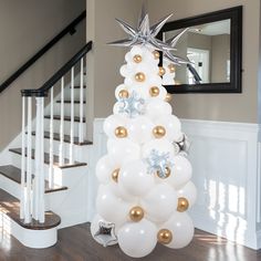 a white christmas tree decorated with gold and silver balloons in front of a stair case