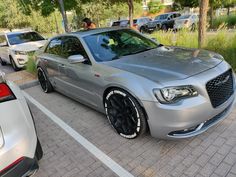 a silver car parked in a parking lot next to other cars and people on the sidewalk