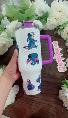 someone is holding a travel mug with cartoon animals on it and flowers in the background