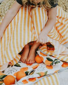 a woman sitting on top of a bed under a blanket with an orange print covering it