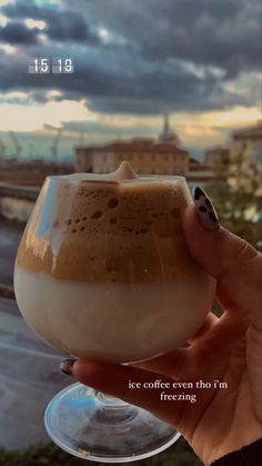 someone is holding up a cup of coffee in front of the cityscape and sky