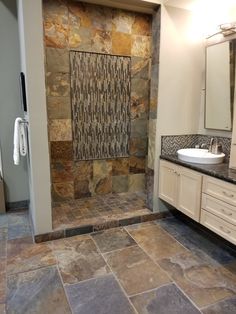 a bathroom with stone walls and flooring in the shower area, along with two sinks