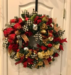 a christmas wreath hanging on the front door with red, gold and green decorations around it