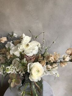 a glass vase filled with white flowers on top of a marble table next to a gray wall