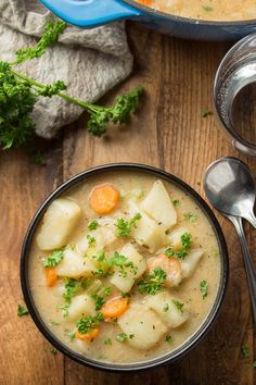 a bowl filled with potatoes and carrots on top of a wooden table next to a spoon