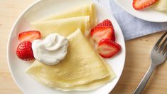 two white plates topped with crepes covered in whipped cream and strawberries next to a fork