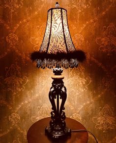 a lamp on a table in front of a wall with damask and floral designs