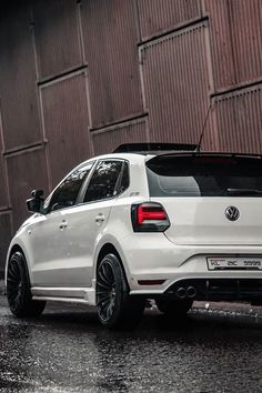 the rear end of a white volkswagen car parked in front of a building on a rainy day