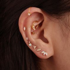 a woman wearing gold ear piercings with opal stones and pearls on her ears