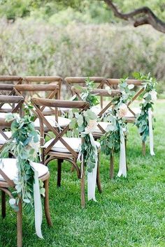 rows of wooden chairs decorated with greenery and ribbons for an outdoor ceremony in the grass