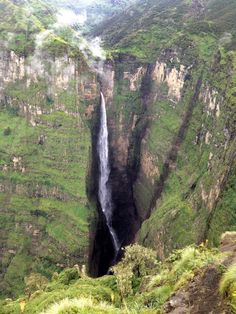 a large waterfall in the middle of a lush green valley