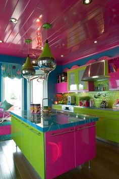 a kitchen with pink, green and blue cabinets in the center is decorated with chandeliers