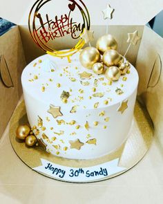 a white and gold birthday cake in a cardboard box with golden stars on the side