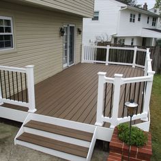 a wooden deck with white railings next to a house