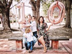 a family sitting on a park bench holding up large balloons