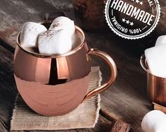 a copper mug filled with marshmallows on top of a wooden table