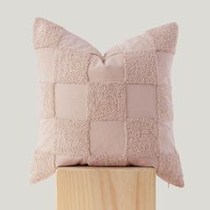 a pink pillow sitting on top of a wooden block with a light colored pillow behind it