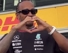 a man making a heart sign with his hands in front of him and wearing sunglasses