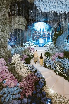 two people walking down a flower covered walkway in front of a stage with flowers all around