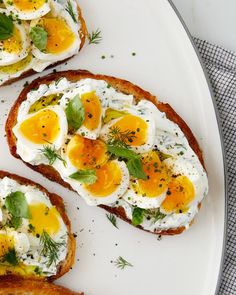 three pieces of toast with eggs and herbs on top, sitting on a white plate