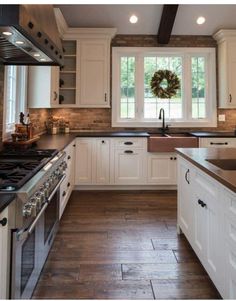 a kitchen with white cabinets and black counter tops, wood flooring and a wreath on the window sill