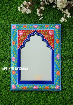 a mirror sitting on top of green grass next to some white and pink flowers in the background