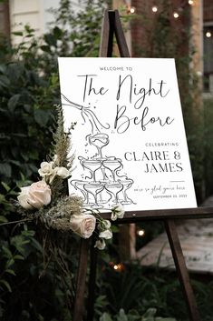 a sign with flowers on it sitting in front of some bushes and lights at night