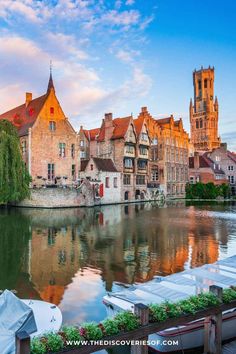 an old town with boats on the river in front of it and some buildings near by