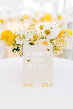 a white table with flowers and a card on it that says, brinnie's first bee day