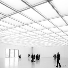 many people are walking around in an empty room with white walls and beams on the ceiling