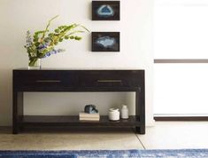 a vase with flowers on top of a wooden table next to two pictures and a rug