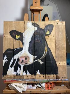 a painting of a black and white cow on a wooden pallet