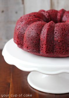 a red velvet bundt cake sitting on top of a white cake platter with one slice cut out