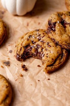 two chocolate chip cookies with one broken in half on parchment paper next to a white pumpkin