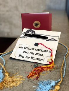 a graduation cap sitting on top of a table next to a red book and tassel