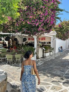 a woman in a blue and white dress is walking down the street by some tables