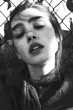 black and white photograph of a woman with her eyes closed behind a chain link fence