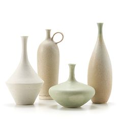 five different vases are lined up in a row on a white surface, one is green and the other is beige