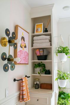 an organized closet with plants and towels on shelves in front of the door to the bathroom