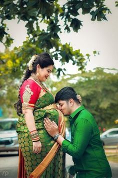 a man kneeling down next to a woman in a green sari and red blouse