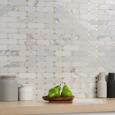 two green pears sit on a wooden plate in front of a white marble wall