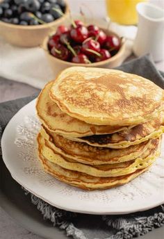 a stack of pancakes sitting on top of a white plate with cherries in the background