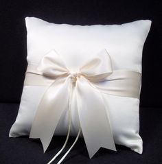 a white pillow with a bow on the front and back of it, sitting on a black background