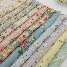 a bunch of different colored fabrics sitting on top of a white table next to flowers