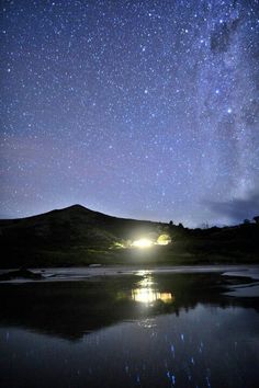 the night sky is filled with stars and light reflecting off water in front of a mountain