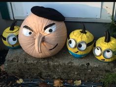 three pumpkins with faces painted on them sitting in front of a door and some plants