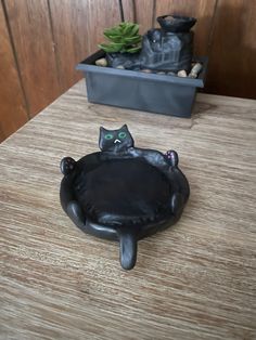 a black cat statue sitting on top of a wooden table next to a potted plant