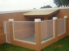 a fenced in area next to a building with grass on the ground and a roof