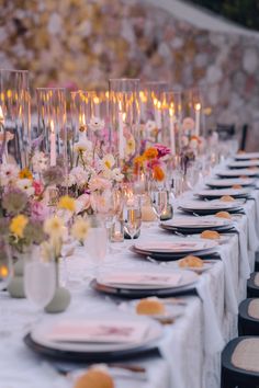 a long table is set with white and pink flowers, silverware, and candles